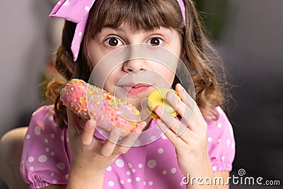 Cute little girl in pink dress holding macaron and donut in hands by the face. Funny concept with sweets. Adolescent Stock Photo