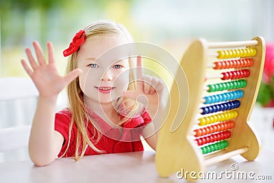 Cute little girl playing with abacus at home. Smart child learning to count. Stock Photo