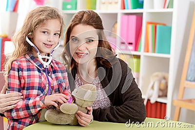 Cute little girl playing nurse, inspecting teddy bear Stock Photo