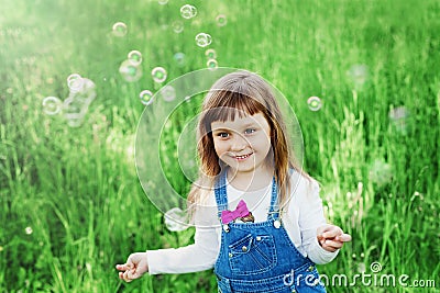 Cute little girl playing with soap bubbles on the green lawn outdoor, happy childhood concept, child having fun Stock Photo