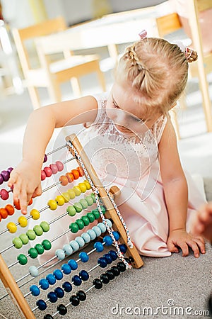 Cute little girl playing with wooden abacus at home. Smart child learning to count. Preschooler having fun with educational toy at Stock Photo