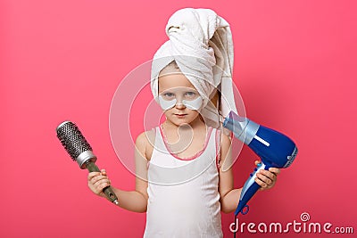 Cute little girl posing with round brush dryer and hairdryer in hands, serious little cute female with patches under eyes and Stock Photo