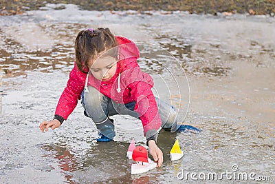 Cute little girl in rain boots playing with colorful ships in the spring creek standing in water Stock Photo