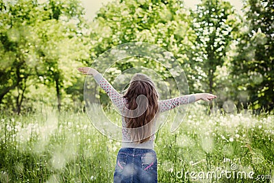 Cute little girl with the raised hands in air standing against the magic nature in sunny day Stock Photo