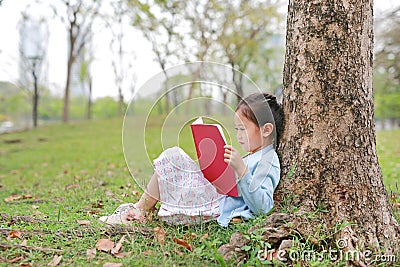 Cute little girl reading book in summer park outdoor lean against tree trunk in the summer garden Stock Photo