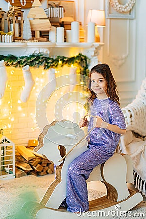 cute little girl on a rocking horse by the fireplace with Christmas decorations. Stock Photo