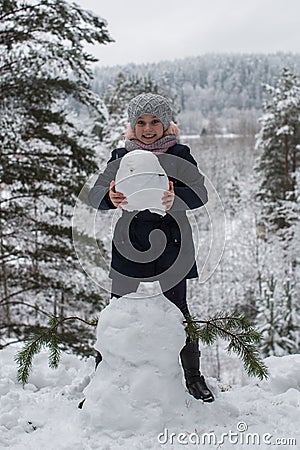Cute girl sculpts snowman in winter snowy Park. Stock Photo