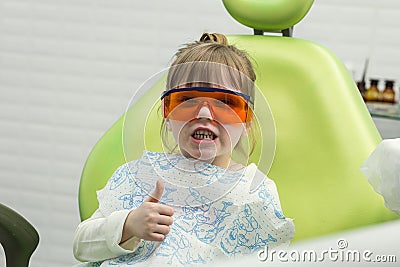 Cute little girl showing thumb up sign at dentist`s office clin Stock Photo