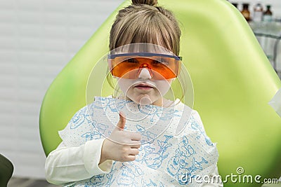 Cute little girl showing thumb up sign at dentist`s office clin Stock Photo