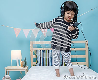 Cute little girl sing a song with smartphone in her bedroom, Happy asian child little girl listening the music with headphone on Stock Photo