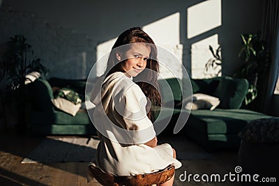 Cute little girl sitting on chair and posing. Smiling caucasian kid look over the shoulder. Stock Photo