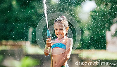 Cute little girl sprinkling with water for herself from the hose, making a rain pleasure for hot summer days. Careless childhood Stock Photo