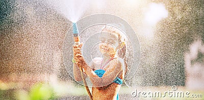 Cute little girl sprinkls a water for herself from the hose, makes a rain. pleasure for hot summer days Stock Photo