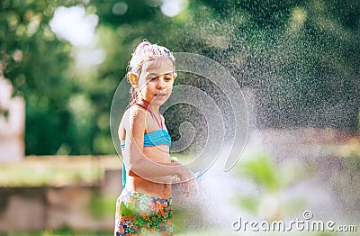 Cute little girl sprinkls a water for herself from the hose, makes a rain. pleasure for hot summer days. Happy careless childhood Stock Photo