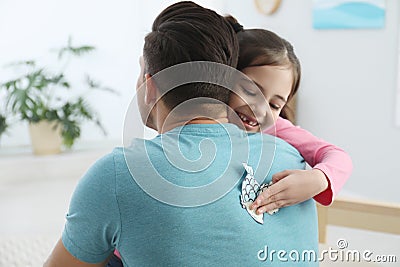 Cute little girl sticking paper fish to father`s back at home Stock Photo