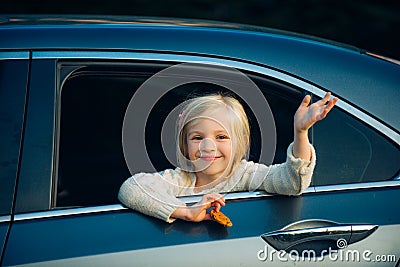 Cute little girl traveling in the car and observing nature from open window. Little girl waving hand for good bye in the Stock Photo