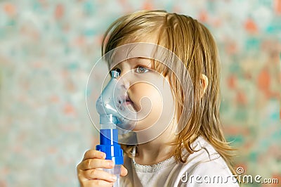 A cute little girl is undergoing medical inhalation treatment with a nebulizer at home. The girl is sitting and doing cough treatm Stock Photo