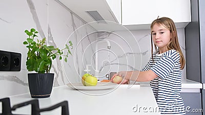 A cute little girl is washing fruits in a modern kitchen with her brother. Children at home. Stock Photo