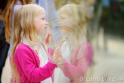 Cute little girl watching animals at the zoo on warm and sunny summer day. Child watching zoo animals through the window. Stock Photo