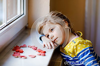 Cute little girl by window with lots of dough hearts as gift for Valentine& x27;s day, Mother& x27;s day or birthday. Adorable Stock Photo