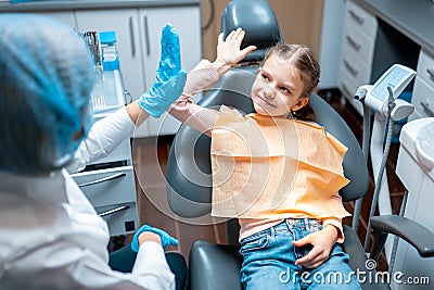 Friendly dentist giving high five little girl patient sitting on dental chair after examination Stock Photo