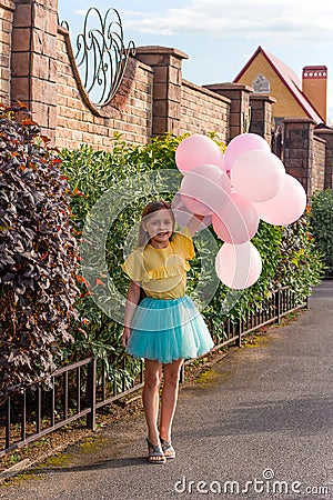 little girl in yellow shirt and blue skirt smiling and holding a lot of balloons ,happy childhood and summer concept Stock Photo