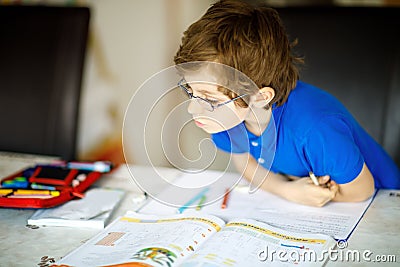 Cute little kid boy with glasses at home making homework, writing letters with colorful pens. Stock Photo