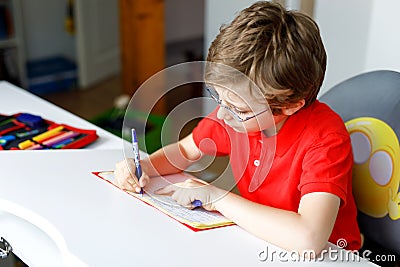Cute little kid boy with glasses at home making homework, writing letters with colorful pens. Stock Photo