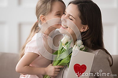 Kid daughter holding flowers kissing congratulating mom with mothers day Stock Photo