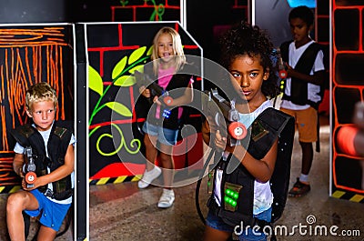 Cute little mulatto girl standing with laser pistol in dark lasertag room during game with friends Stock Photo