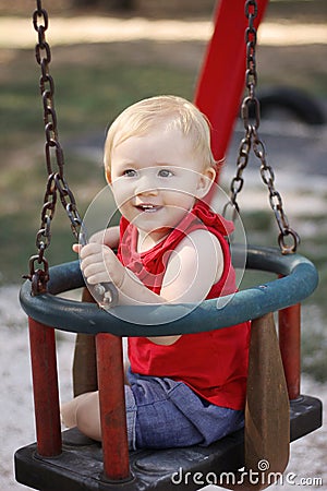 Baby girl smiling and sitting on the swing in the park Stock Photo