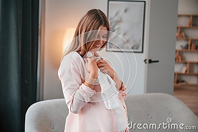 Cute little shirt. Beautiful pregnant woman is indoors at home Stock Photo