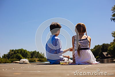 Cute little siblings sitting on pier and having snacks Stock Photo