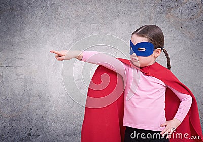 Cute little super hero girl in the red cloak against the gray wall Stock Photo