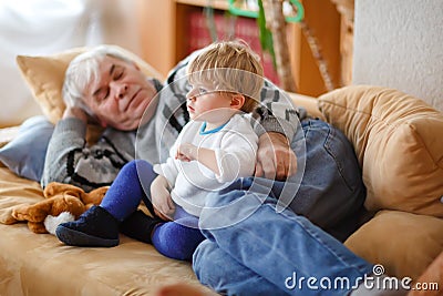 Cute little toddler boy and grandfather watching together tv show. Baby grandson and happy retired senior man sitting Stock Photo