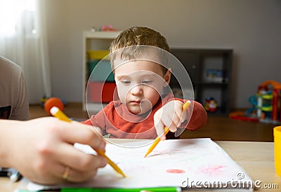 A cute little toddler boy of two years old with dad draws with markers in the album Stock Photo