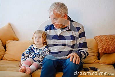 Cute little toddler girl and grandfather watching together tv show. Baby granddaughter and happy retired senior man Stock Photo