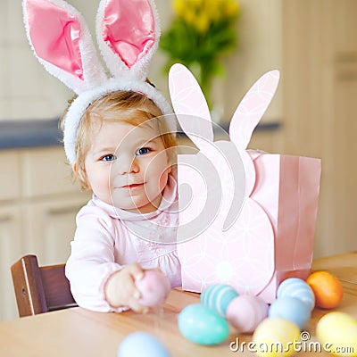 Cute little toddler girl wearing Easter bunny ears playing with colored pastel eggs. Happy baby child unpacking gifts Stock Photo