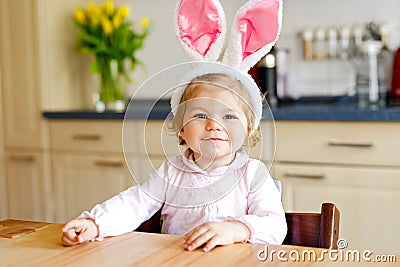 Cute little toddler girl wearing Easter bunny ears playing with colored pastel eggs. Happy baby child unpacking gifts Stock Photo