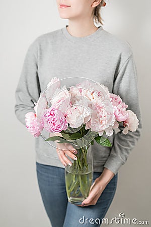 Cute and lovely peony flowers in women`s hands.. many layered petals. Bunch pale pink peonies flowers light gray Stock Photo