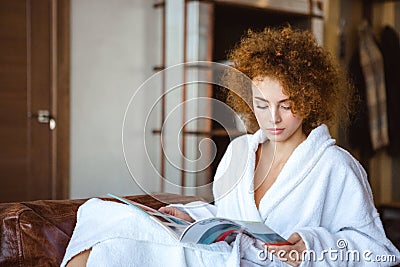 Cute lovely serene female sitting at home and reading magazine Stock Photo