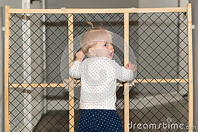 Cute Baby Standing Next to Safety Gate at Home Stock Photo