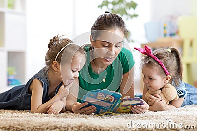 Cute mother and her two daughters children reading story together Stock Photo