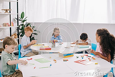 cute multiethnic preschoolers sculpturing figures with plasticine at tables Stock Photo