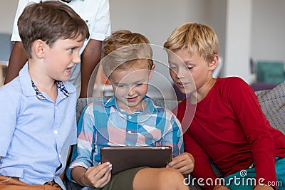 Cute multiracial elementary schoolboys looking at digital tablet while sitting on couch in school Stock Photo