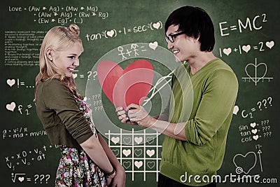 Cute nerd guy and girl holding heart in classroom Stock Photo