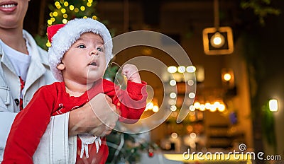 Cute newborn baby boy next to a Christmas tree with festive decoration and ferry lights for New Year celebration Stock Photo