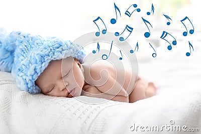 Cute newborn baby in knitted hat sleeping on bed and flying music notes. Stock Photo