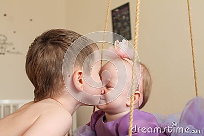 Cute older brother kisses little sister who is swinging on a swing Stock Photo
