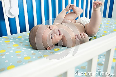 Cute one month old newborn baby is laying on her back in the crib, crying. Stock Photo